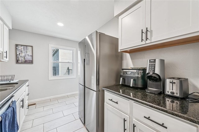 kitchen featuring dishwasher, dark stone countertops, white cabinetry, and freestanding refrigerator