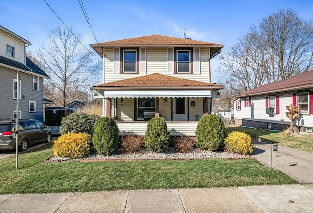 traditional style home with covered porch, a shingled roof, and a front lawn