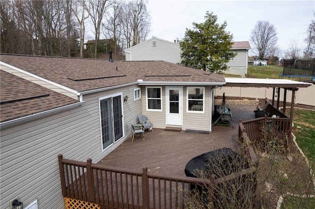 rear view of property featuring a wooden deck, a trampoline, and roof with shingles