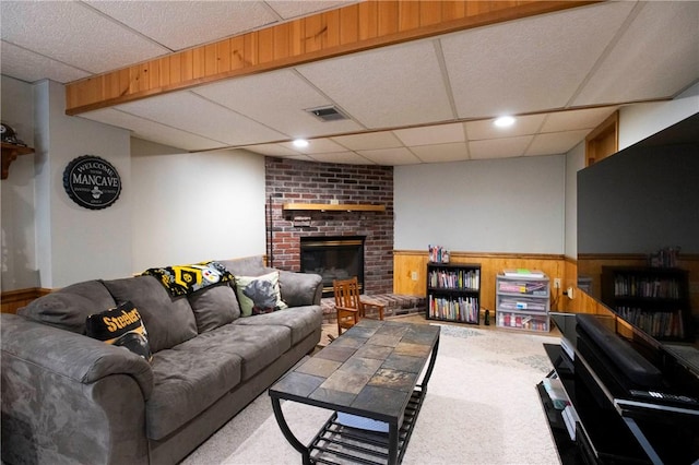 carpeted living area featuring a wainscoted wall, visible vents, a paneled ceiling, wood walls, and a brick fireplace