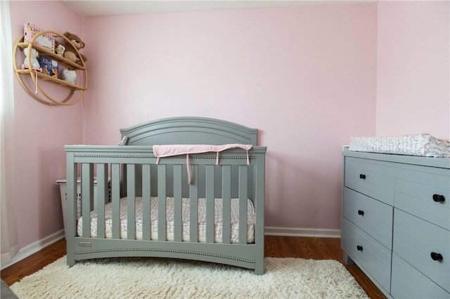bedroom featuring a crib, wood finished floors, and baseboards
