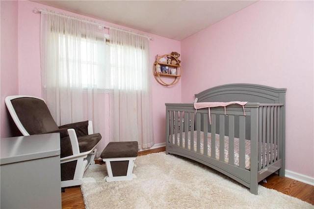 bedroom featuring a crib, baseboards, and wood finished floors