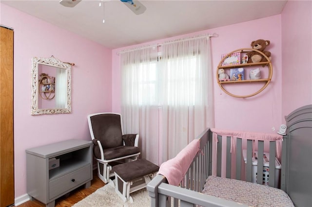 bedroom with a nursery area, wood finished floors, and a ceiling fan