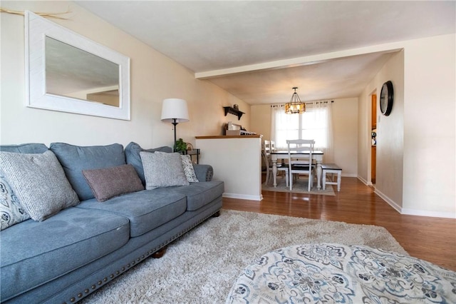 living room featuring an inviting chandelier, wood finished floors, baseboards, and beam ceiling