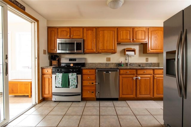 kitchen featuring dark stone counters, light tile patterned floors, brown cabinetry, and stainless steel appliances