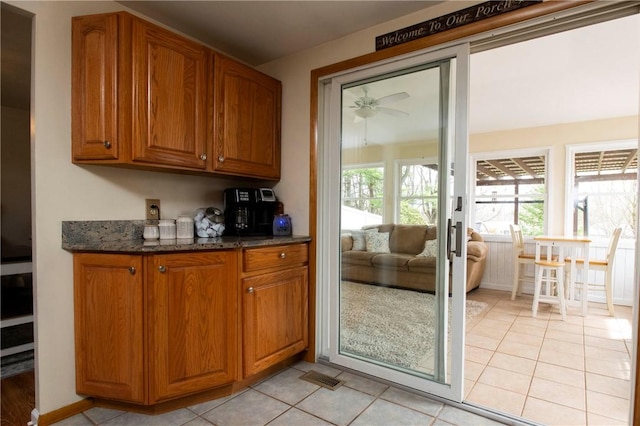 kitchen with dark stone countertops, light tile patterned flooring, brown cabinetry, and visible vents
