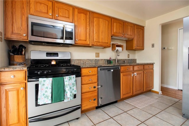 kitchen with dark stone countertops, brown cabinetry, appliances with stainless steel finishes, and a sink