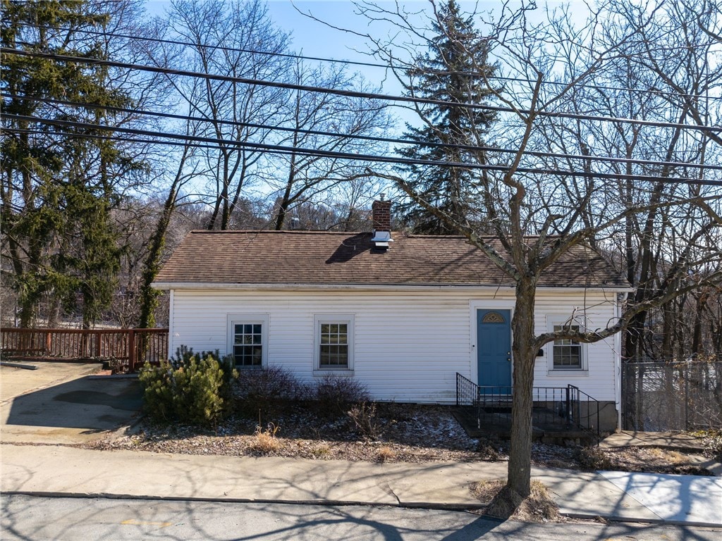 view of property exterior with entry steps, a chimney, roof with shingles, and fence