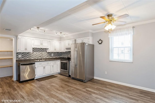 kitchen with dark countertops, backsplash, stainless steel appliances, white cabinetry, and a ceiling fan
