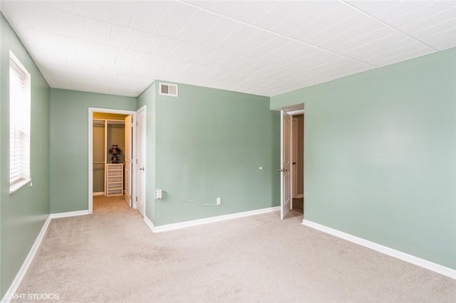 unfurnished bedroom with visible vents, a walk in closet, a closet, carpet floors, and baseboards