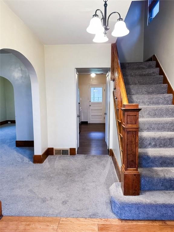 stairs featuring visible vents, carpet, baseboards, arched walkways, and a notable chandelier
