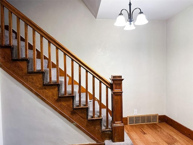 staircase featuring baseboards, visible vents, wood finished floors, and an inviting chandelier