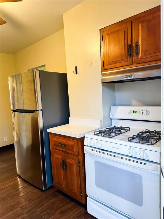 kitchen with light countertops, freestanding refrigerator, brown cabinetry, under cabinet range hood, and white gas stove