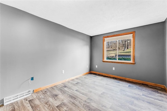 unfurnished room with wood finished floors, visible vents, and baseboards