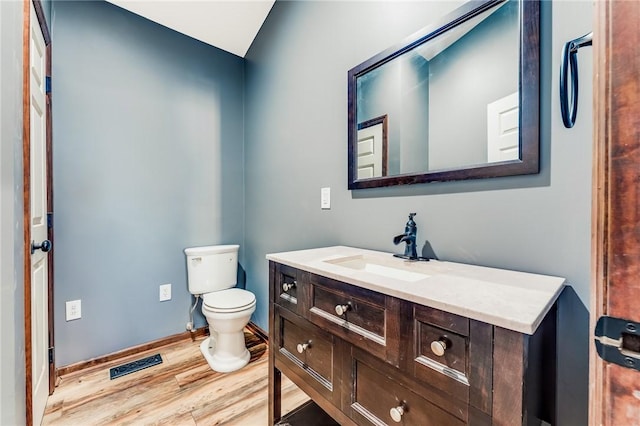 half bath with visible vents, toilet, wood finished floors, baseboards, and vanity