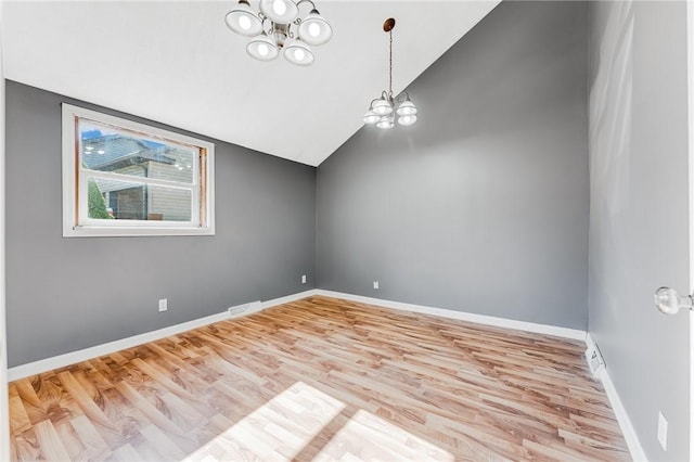 empty room featuring visible vents, a notable chandelier, lofted ceiling, wood finished floors, and baseboards