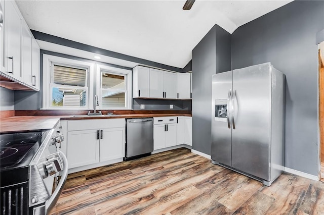 kitchen with light wood-type flooring, a sink, appliances with stainless steel finishes, white cabinets, and vaulted ceiling