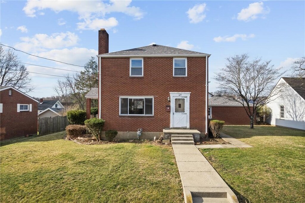 view of front of house featuring brick siding, a chimney, a front lawn, and fence