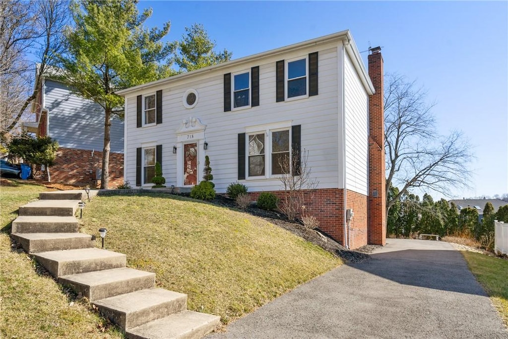 colonial home featuring brick siding, aphalt driveway, a front yard, and a chimney