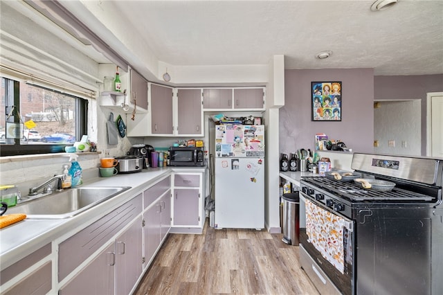 kitchen with a sink, freestanding refrigerator, stainless steel gas range, light wood finished floors, and black microwave