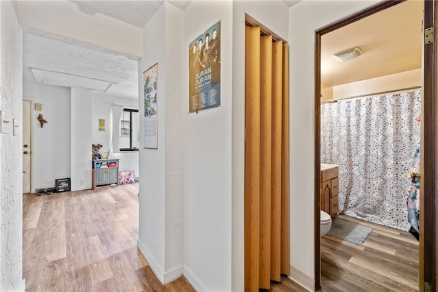hallway with visible vents, baseboards, and wood finished floors