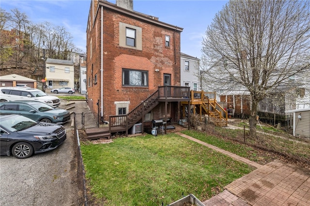 rear view of house featuring a chimney, stairway, a deck, brick siding, and a yard