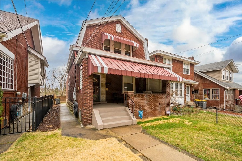 view of front of property with brick siding, a porch, a front lawn, and fence