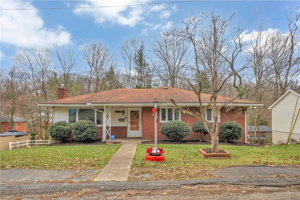 view of front of house with brick siding, a chimney, a front yard, and fence
