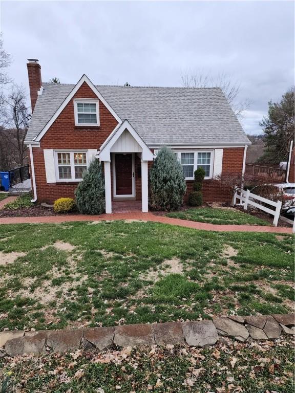 view of front of house with a front yard, fence, roof with shingles, a chimney, and brick siding