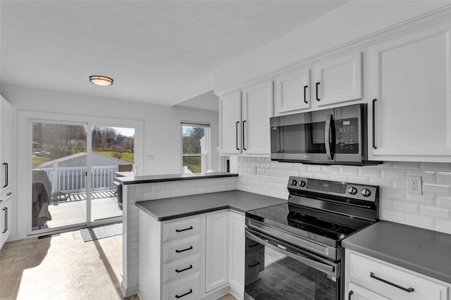 kitchen featuring white cabinetry, dark countertops, a peninsula, and appliances with stainless steel finishes