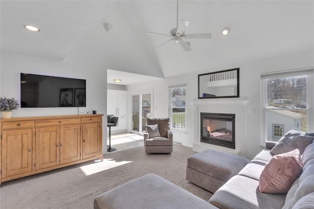 living area with a ceiling fan, high vaulted ceiling, recessed lighting, light carpet, and a glass covered fireplace