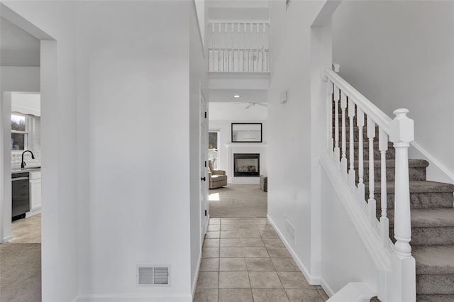 corridor with visible vents, light carpet, stairway, light tile patterned floors, and a towering ceiling