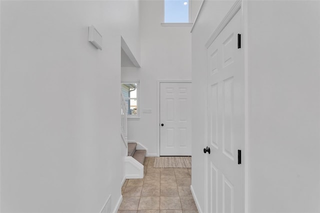 corridor with light tile patterned flooring, stairway, baseboards, and a towering ceiling