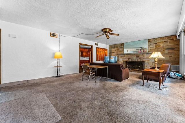 carpeted living room featuring a textured ceiling, a stone fireplace, ceiling fan, and a textured wall