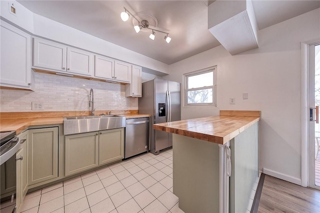 kitchen featuring a peninsula, a sink, decorative backsplash, appliances with stainless steel finishes, and wood counters