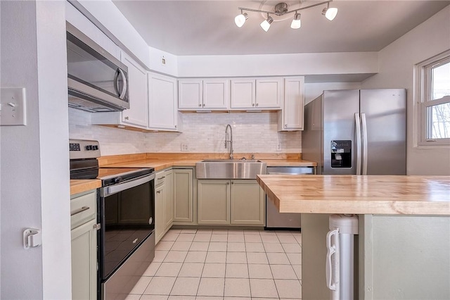 kitchen featuring a sink, stainless steel appliances, light tile patterned floors, decorative backsplash, and wooden counters