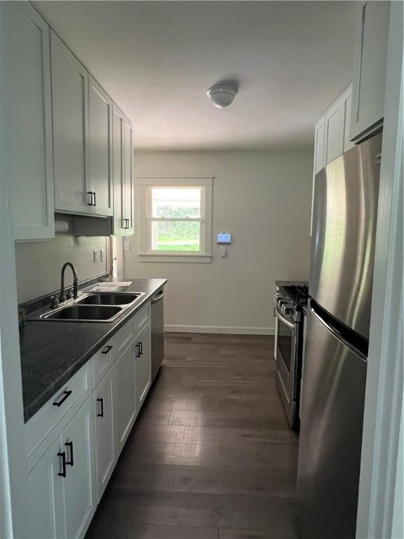 kitchen with a sink, appliances with stainless steel finishes, baseboards, and white cabinets