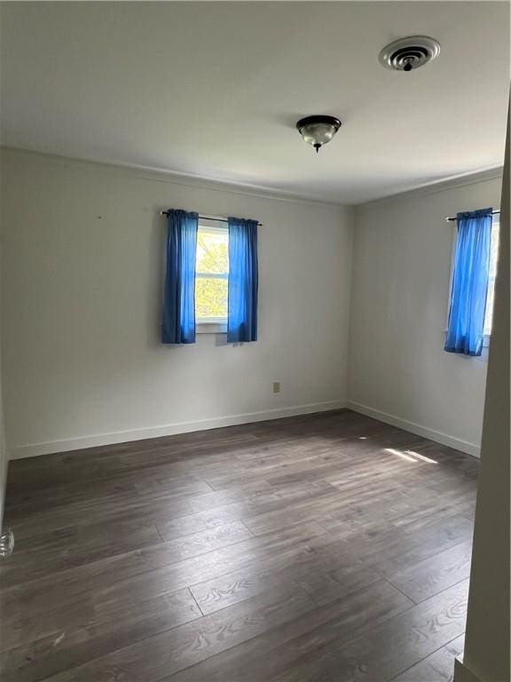 unfurnished room with visible vents, dark wood finished floors, and baseboards