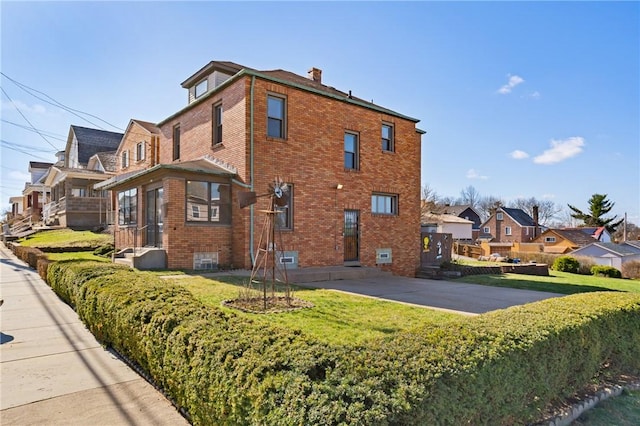 view of side of property featuring a lawn, a chimney, and brick siding