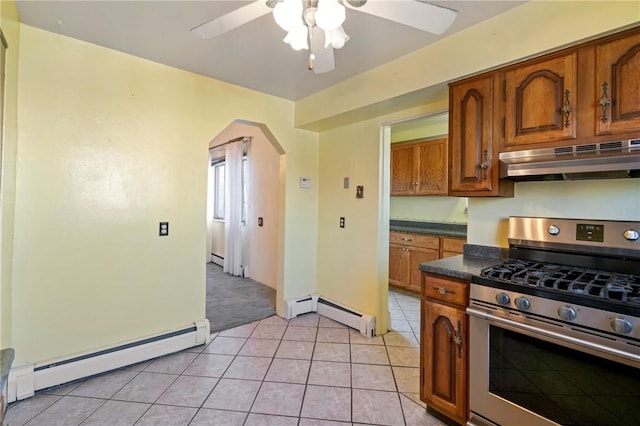 kitchen with stainless steel range with gas stovetop, under cabinet range hood, dark countertops, arched walkways, and a baseboard radiator
