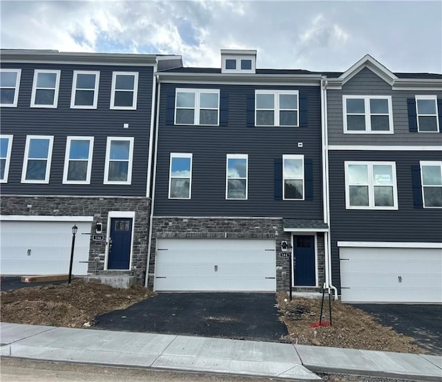 townhome / multi-family property featuring aphalt driveway, stone siding, and an attached garage