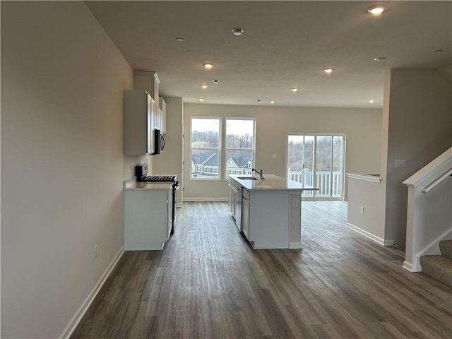 kitchen with a sink, light countertops, dark wood finished floors, a center island with sink, and stainless steel appliances