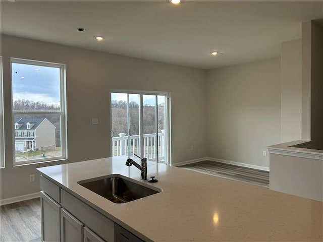 kitchen featuring light wood-style floors, recessed lighting, light stone counters, a sink, and baseboards