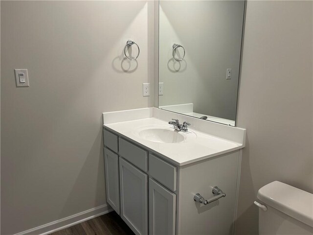 half bath with toilet, wood finished floors, vanity, and baseboards