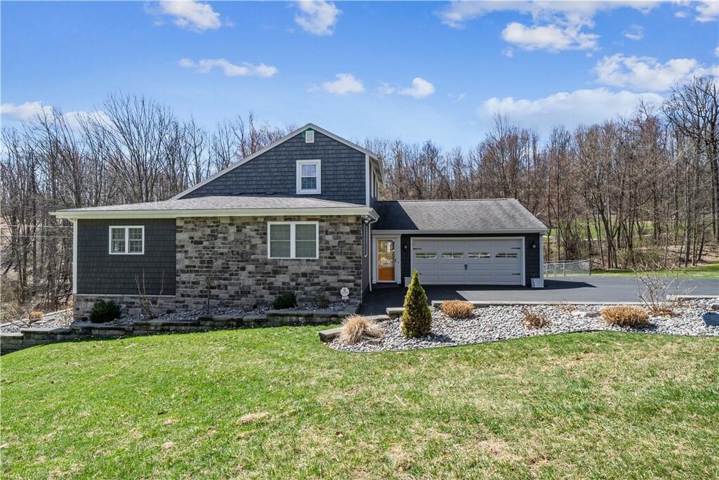 view of front of property featuring driveway, a garage, a front lawn, and stone siding