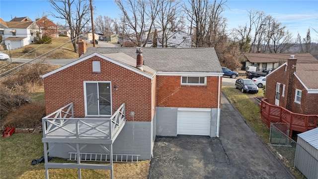 rear view of house with driveway, brick siding, a chimney, and a residential view