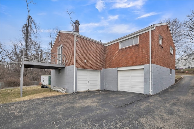 back of house featuring driveway, a chimney, a wooden deck, an attached garage, and brick siding