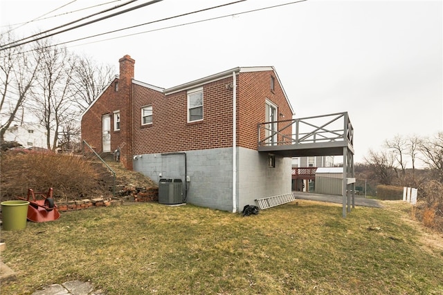 view of side of property with a chimney, a wooden deck, brick siding, central AC, and a yard