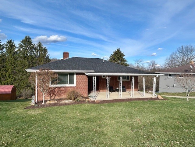 back of house featuring an outbuilding, a lawn, a patio, brick siding, and a chimney