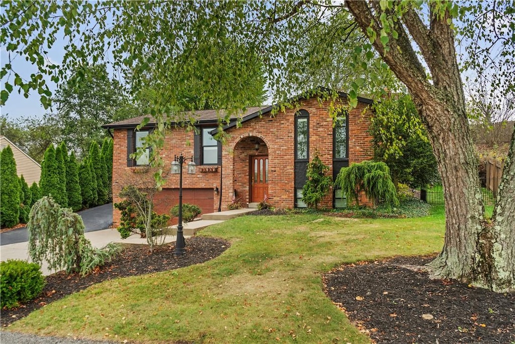 bi-level home with driveway, brick siding, and a front lawn